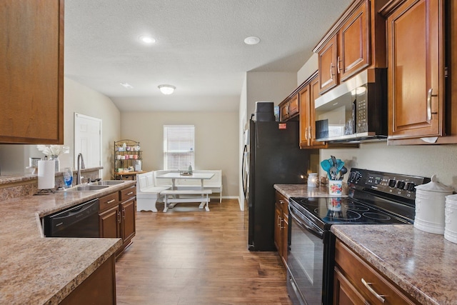 kitchen with black appliances, a sink, dark wood finished floors, and brown cabinets