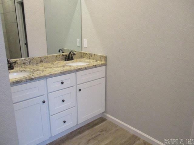 bathroom with double vanity, wood finished floors, a sink, and baseboards