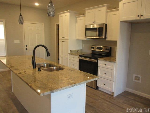 kitchen with stainless steel appliances, a sink, a center island with sink, and white cabinets