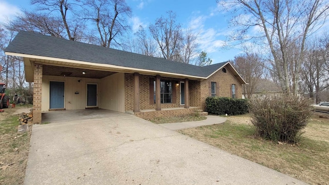 ranch-style home featuring a carport, concrete driveway, brick siding, and roof with shingles