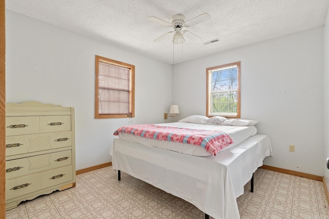 bedroom with a ceiling fan, visible vents, a textured ceiling, and baseboards