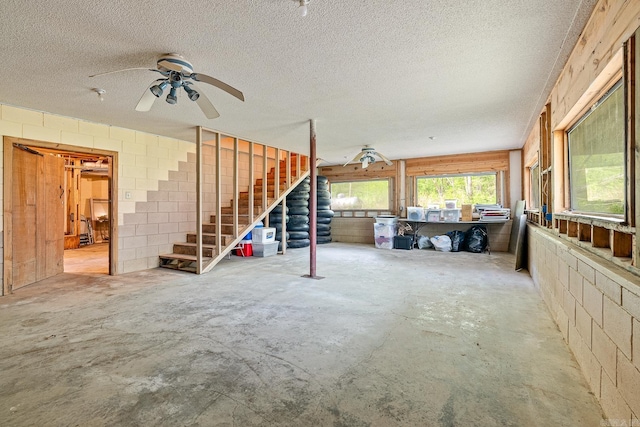 interior space with concrete block wall, a ceiling fan, unfinished concrete flooring, stairs, and a textured ceiling