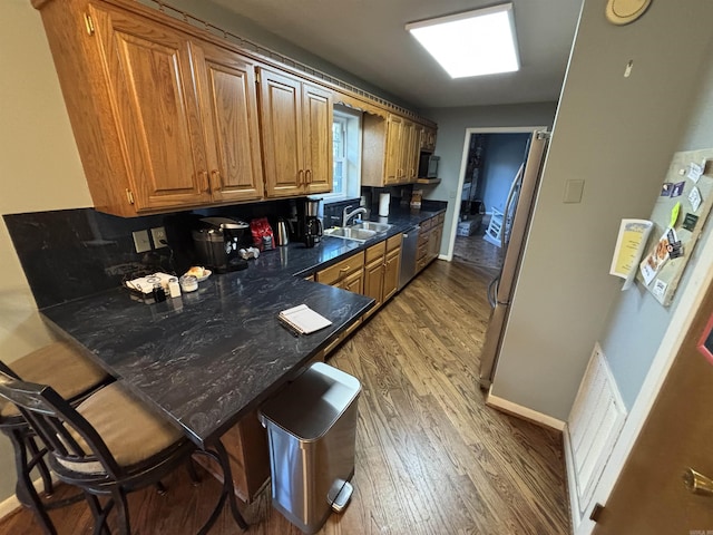 kitchen featuring dark wood-style floors, a breakfast bar, appliances with stainless steel finishes, a sink, and a peninsula