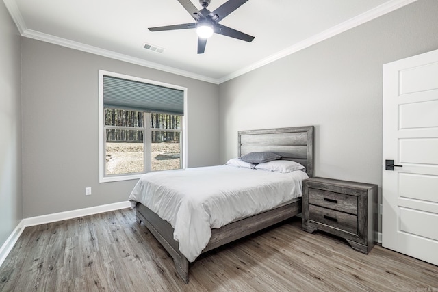 bedroom with crown molding, visible vents, light wood-style flooring, a ceiling fan, and baseboards
