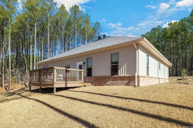 back of property featuring a shingled roof, brick siding, a yard, and a deck