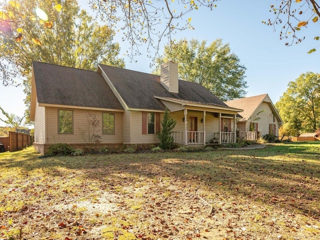 view of front of house with covered porch, a chimney, a front yard, and fence