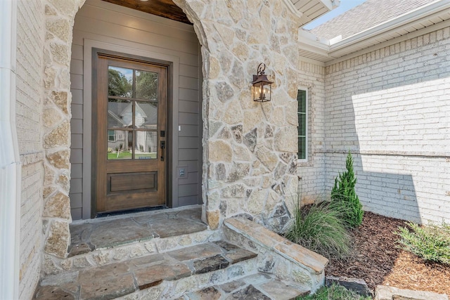 view of exterior entry featuring stone siding, brick siding, and roof with shingles