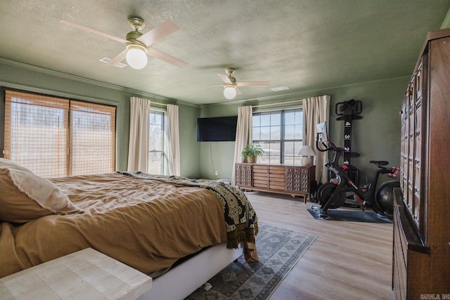 bedroom featuring a ceiling fan, light wood-type flooring, crown molding, and a textured ceiling