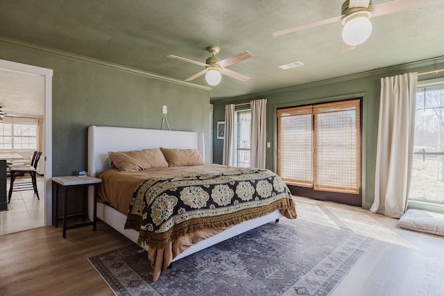 bedroom featuring visible vents, ceiling fan, wood finished floors, access to exterior, and crown molding