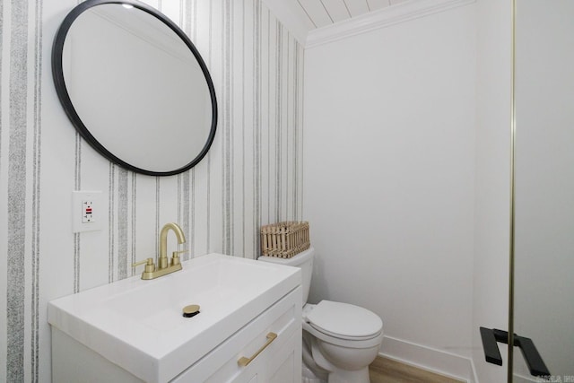 half bath featuring toilet, wood finished floors, vanity, baseboards, and crown molding