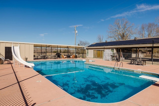 view of pool featuring a water slide, fence, a diving board, a fenced in pool, and a patio area