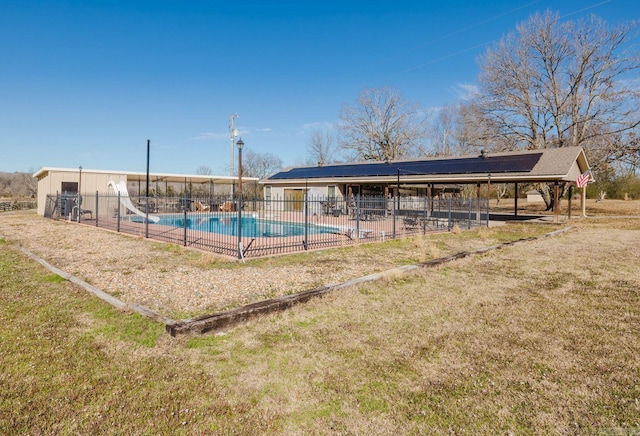 community pool featuring a water slide, fence, and a lawn