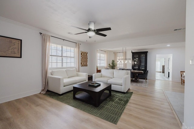 living area featuring ceiling fan, visible vents, baseboards, light wood-style floors, and ornamental molding