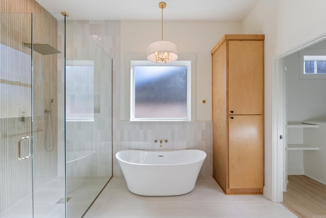 full bathroom featuring tile walls, tile patterned flooring, a freestanding bath, a shower stall, and a closet