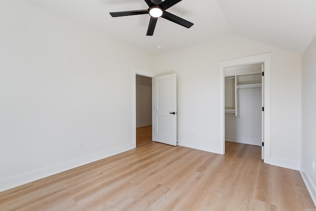 unfurnished bedroom featuring baseboards, a spacious closet, lofted ceiling, and light wood-style floors