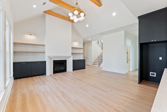 unfurnished living room featuring stairs, light wood-type flooring, a glass covered fireplace, and an inviting chandelier