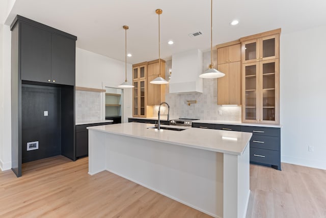 kitchen featuring light wood finished floors, custom range hood, decorative backsplash, and a sink