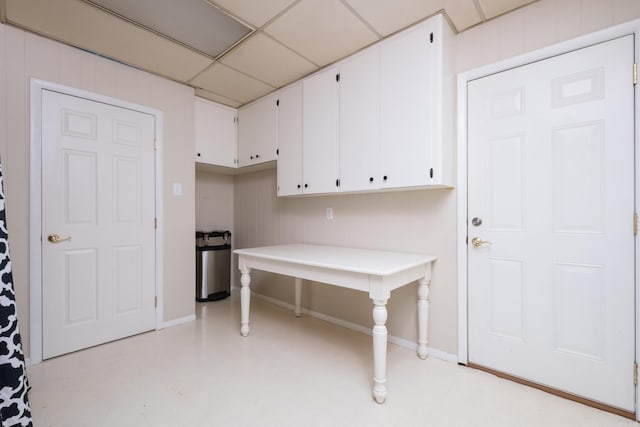 interior space with light floors, a paneled ceiling, light countertops, white cabinetry, and baseboards