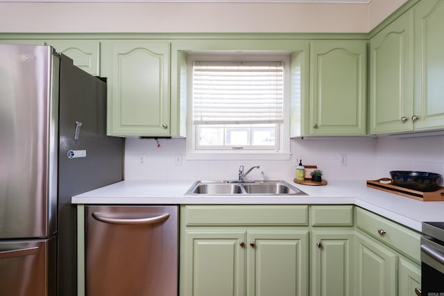 kitchen with a sink, light countertops, appliances with stainless steel finishes, backsplash, and green cabinetry