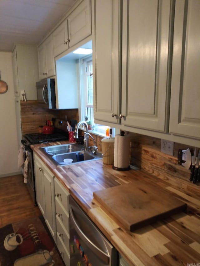 kitchen featuring white cabinets, appliances with stainless steel finishes, wooden counters, and a sink