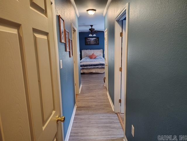 hall featuring ornamental molding, a textured wall, baseboards, and wood finished floors