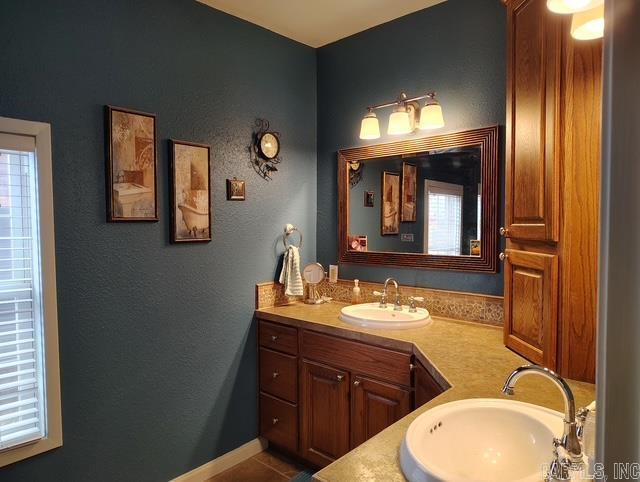 full bath featuring double vanity, tile patterned floors, a sink, and baseboards