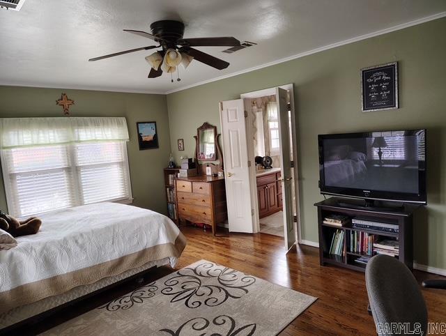 bedroom with baseboards, wood finished floors, visible vents, and crown molding