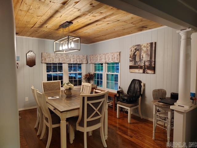 dining space featuring a notable chandelier, wood finished floors, wood ceiling, baseboards, and decorative columns