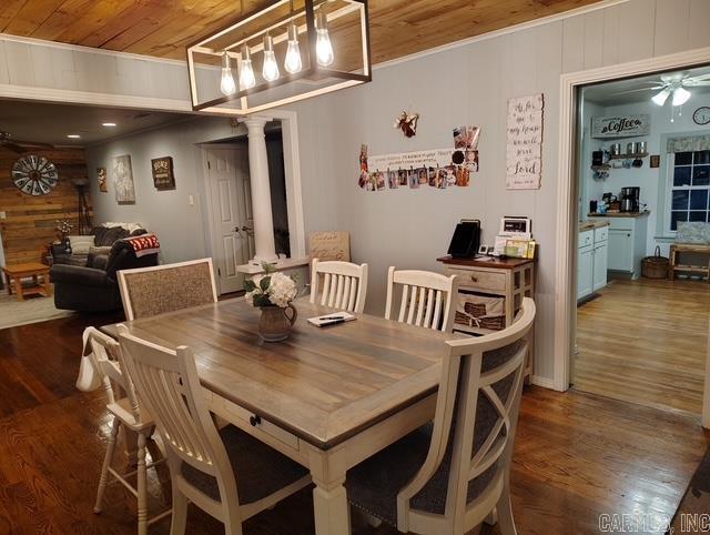 dining area featuring a ceiling fan, wood ceiling, wood walls, wood finished floors, and ornate columns