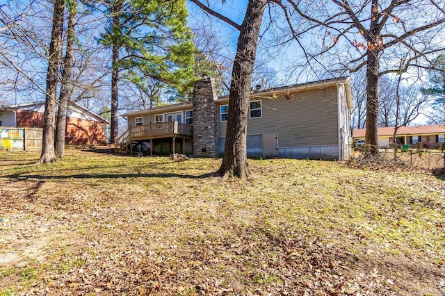 back of property featuring fence, a chimney, a wooden deck, and a lawn