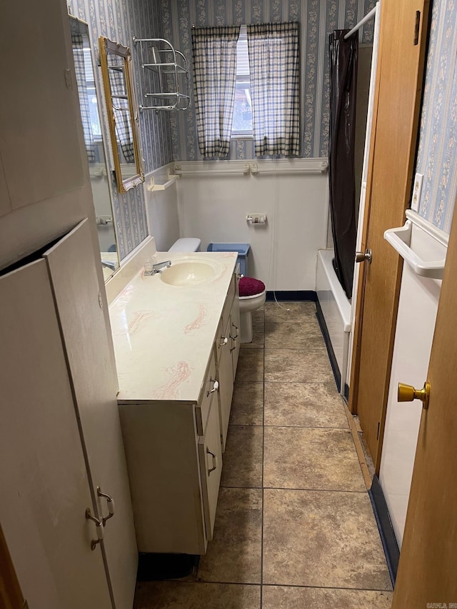 bathroom featuring toilet, vanity, baseboards, shower / tub combo with curtain, and wallpapered walls