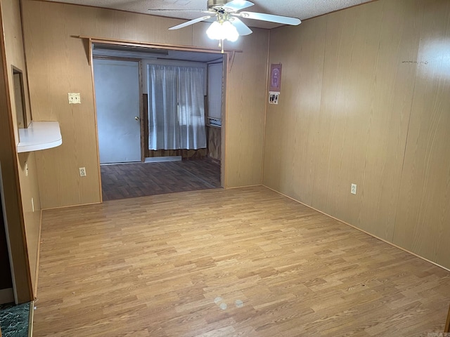 unfurnished room featuring wood walls, wood finished floors, and a ceiling fan