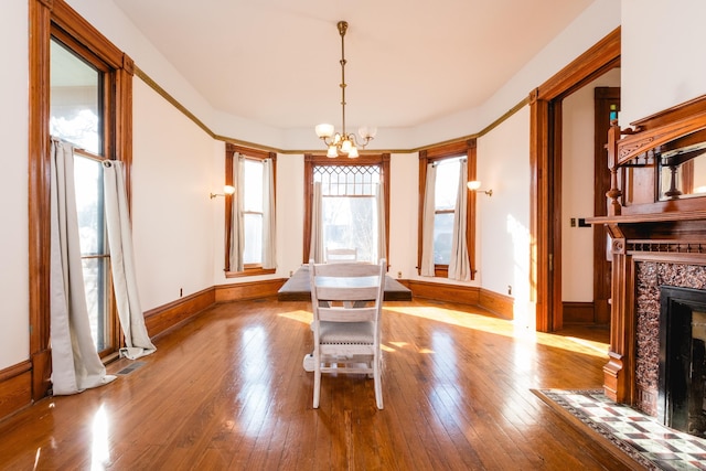 unfurnished dining area with baseboards, a fireplace, hardwood / wood-style floors, and an inviting chandelier