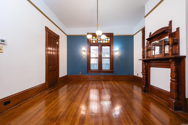 empty room featuring wood-type flooring, a chandelier, and baseboards