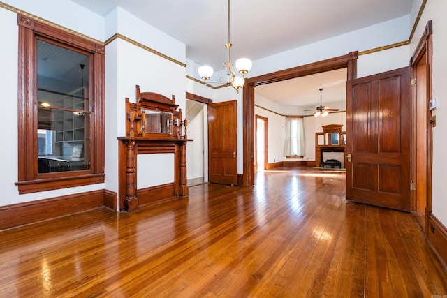 unfurnished living room featuring wood-type flooring, baseboards, and ceiling fan with notable chandelier