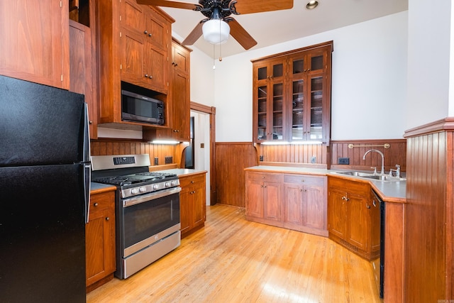 kitchen with a wainscoted wall, freestanding refrigerator, a sink, gas range, and light wood-type flooring