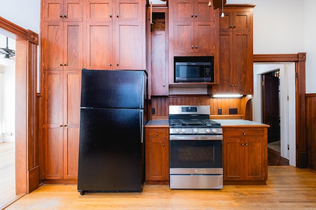 kitchen featuring light wood finished floors, light countertops, brown cabinetry, freestanding refrigerator, and stainless steel gas range oven