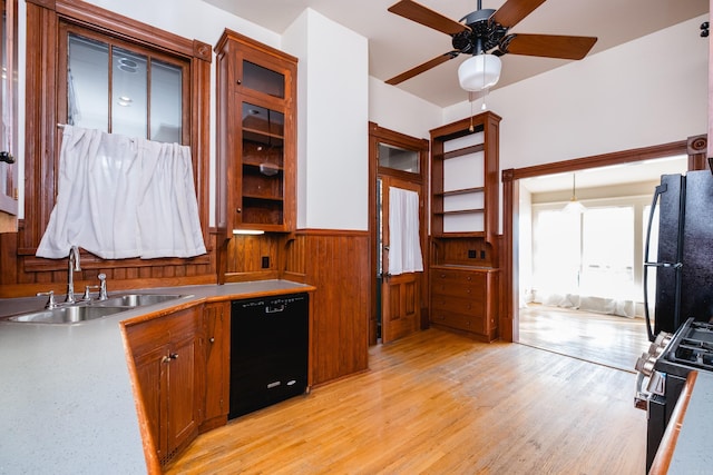 kitchen featuring brown cabinets, light wood finished floors, wainscoting, a sink, and black appliances