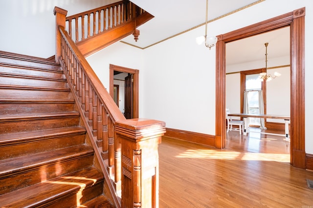 staircase featuring wood finished floors, visible vents, baseboards, an inviting chandelier, and crown molding