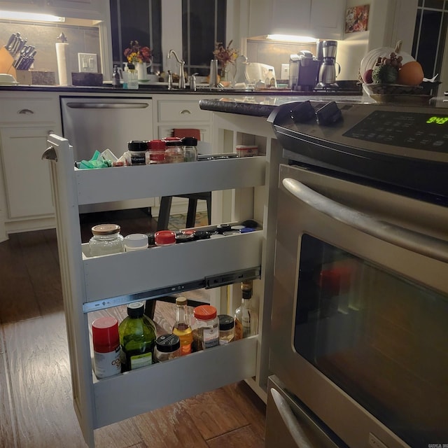 interior space with stainless steel appliances, dark countertops, wood finished floors, and white cabinetry