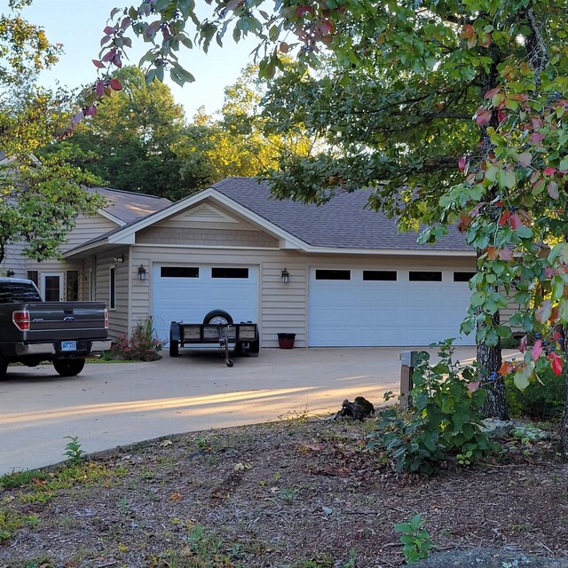 view of front facade with a shingled roof, driveway, and an attached garage