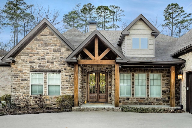 view of front of home featuring stone siding, a shingled roof, a chimney, and french doors