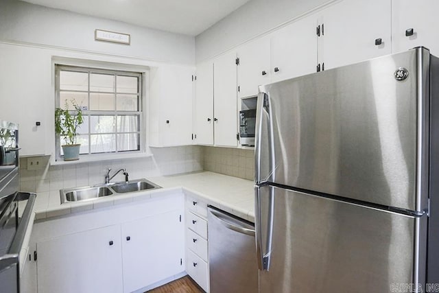 kitchen with stainless steel appliances, tasteful backsplash, white cabinets, a sink, and wood finished floors