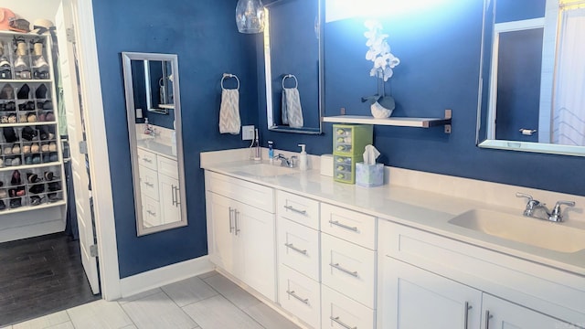 bathroom featuring a walk in closet, a sink, baseboards, and double vanity