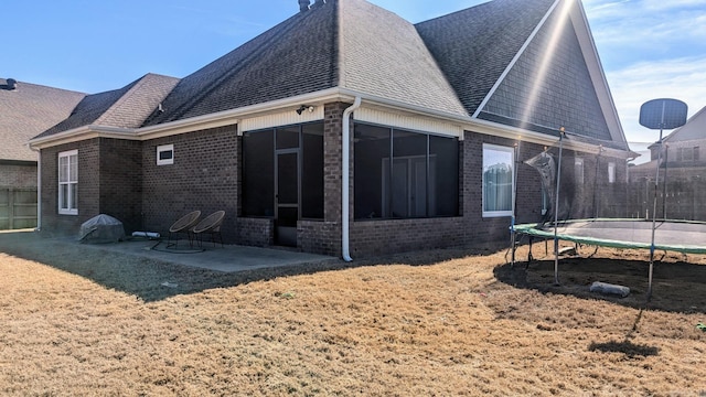 rear view of house with brick siding, a trampoline, a patio area, and a shingled roof