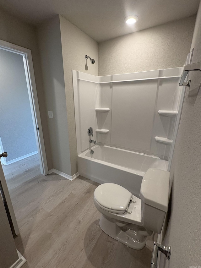 full bathroom with shower / bathing tub combination, wood finished floors, baseboards, toilet, and a textured wall