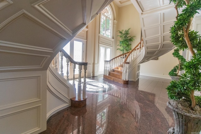 entrance foyer with a decorative wall, granite finish floor, baseboards, ornamental molding, and stairway