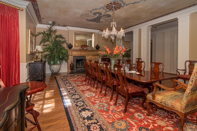 dining area with crown molding, a fireplace, wood finished floors, a chandelier, and ornate columns