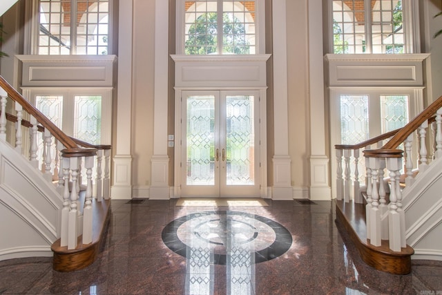 foyer entrance with granite finish floor, stairway, a decorative wall, and french doors