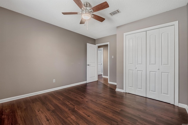 unfurnished bedroom with baseboards, visible vents, dark wood finished floors, a textured ceiling, and a closet